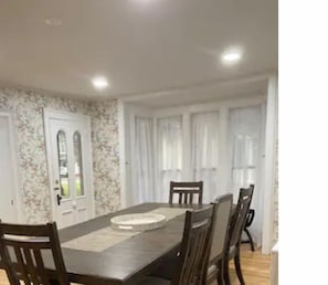 Un coin repas avec une table rectangulaire, six chaises et un mur recouvert d’un papier peint à motifs floraux.