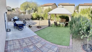 Een achtertuin met een terras, een barbecue, een overdekte zithoek en een kleine tuin.