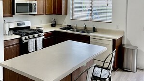 Een moderne keuken met houten kastjes, een roestvrijstalen fornuis, een magnetron en een groot eiland met barstoelen.