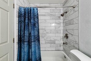 A bathroom with a shower curtain, a bathtub, and tiled walls. - Pool Home W Beautiful Tiki Hut - 3 Bed 3 Bath. 1 mile from beach! (Boca Raton)