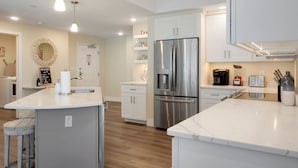 A modern kitchen with white cabinetry, a stainless steel refrigerator, a built-in oven, and a marble countertop. - Luxurious Bay Views steps Boardwalk (Ocean City)
