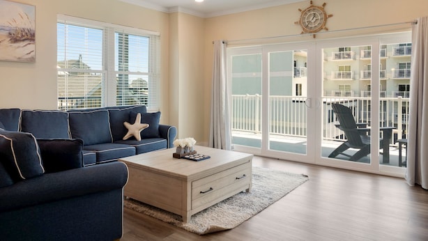 A living room with a blue sofa, a wooden coffee table, and a starfish decoration. There is a ceiling fan and a large window with blinds. - Luxurious Bay Views steps Boardwalk (Ocean City)