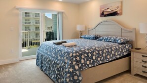 A bedroom with a bed, two bedside tables, a ceiling fan, a window with a view of a building, and a painting on the wall. - Luxurious Bay Views steps Boardwalk (Ocean City)