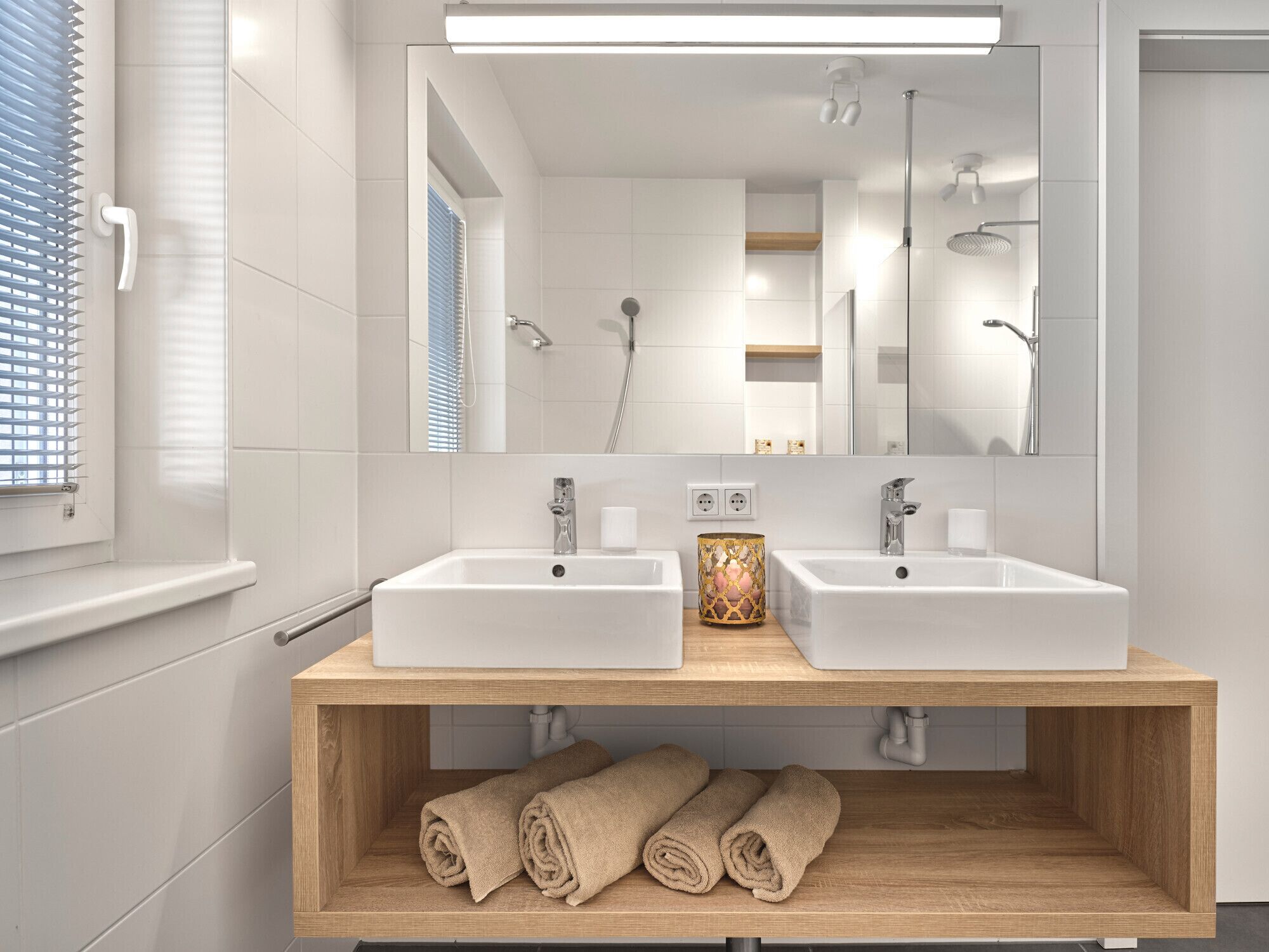 Ein modernes Badezimmer mit zwei Waschbecken, einem Spiegel und einer Holzablage mit Handtüchern.