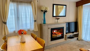 Ein Hotelzimmer mit Holztisch, Stühlen, einem Fernseher, einem Kamin und großen Fenstern mit Vorhängen.