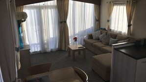 Ein Hotelzimmer mit einer Couch, einem kleinen Tisch, einem Stuhl, einer Küchenzeile und großen Fenstern mit Vorhängen.