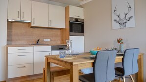 A modern kitchen with white cabinets, a wooden countertop, and a dining area with a table and chairs. - Grimming Lodge Goldrute (Tauplitz)