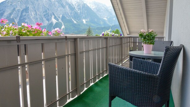 A balcony with a view of mountains, a table with chairs, and potted plants. - Grimming Lodge Goldrute (Tauplitz)