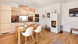 A modern kitchen with wooden cabinets, a dining table set for four, and a fireplace. - Alm Lodge A2 - Tauplitz Lodges (Tauplitz)