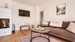 A modern living room with a fireplace, a sofa, a coffee table, and a TV mounted on the wall. - Alm Lodge A2 - Tauplitz Lodges (Tauplitz)