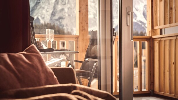 Een gezellige kamer met een bed, een tafel met glazen en uitzicht op bergen door grote glazen deuren.