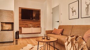 Een moderne woonkamer met een bank, een salontafel, een open haard en een afbeelding van herten in een lijst.
