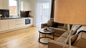 A modern living room with a sofa, a coffee table, and a lamp. There is a kitchen area with cabinets and a sink. - Alm Lodge A8 - Tauplitz Lodges (Tauplitz)