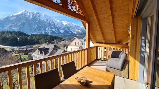 Un balcon en bois, agrémenté d’une table et de chaises, qui offre une vue sur une chaîne de montagnes.
