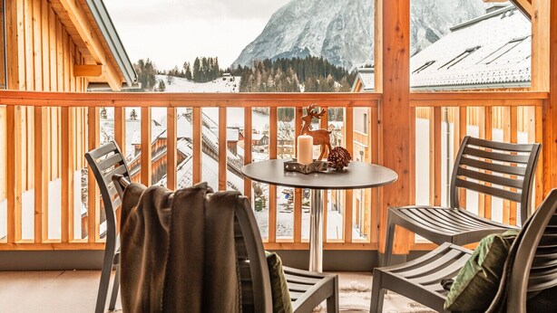 A wooden balcony with a table and chairs, overlooking a snowy mountain landscape. - Alm Lodge A13 - Tauplitz Lodges (Tauplitz)
