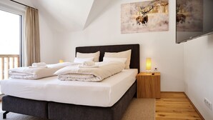 A modern bedroom with a large bed, a nightstand, a TV, and artwork on the wall. - Alm Lodge A13 - Tauplitz Lodges (Tauplitz)