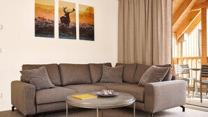 A modern living room with a grey sectional sofa, a round coffee table, and three framed wildlife photographs on the wall. - Alm Lodge A13 - Tauplitz Lodges (Tauplitz)