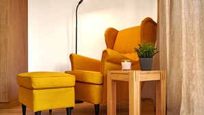 A yellow armchair and ottoman in a room with a wooden floor, a small wooden table with a candle and a plant, and a floor lamp. - Alm Lodge A13 - Tauplitz Lodges (Tauplitz)