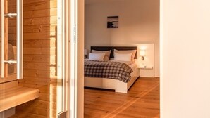 A bedroom with a wooden floor, a bed with a checkered blanket, a nightstand with a lamp, and a wall-mounted picture. - Bergblick Lodge B6 - Tauplitz Lodges (Tauplitz)