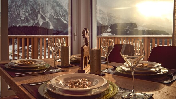 A dining table set for two with a mountain view, a wooden chair, and a candle holder. - Bergblick Lodge B6 - Tauplitz Lodges (Tauplitz)