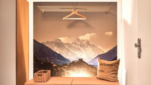 A room with a wooden bench, a hanging clothes rack, a cushion with text, and a wall with a mountain landscape. - Wasserfall Lodge C1 - Tauplitz Lodges (Tauplitz)