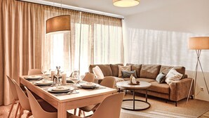 A modern living room with a wooden dining table set for four, a sofa with cushions, and a floor lamp. - Wasserfall Lodge C1 - Tauplitz Lodges (Tauplitz)