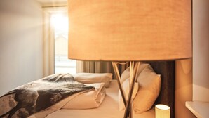 A hotel room with a bed, pillows, a lamp, and a window with curtains. - Wasserfall Lodge C1 - Tauplitz Lodges (Tauplitz)