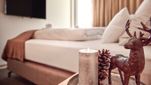 Ein Schlafzimmer mit einem Bett, einem an der Wand befestigten Fernseher, einem Nachttisch mit Kerze, einer Kiefernzapfen und einer Hirschfigur.