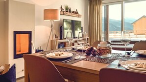 Ein Essbereich mit Holztisch, Stühlen, einem Fernseher und Blick auf Berge durch große Fenster.
