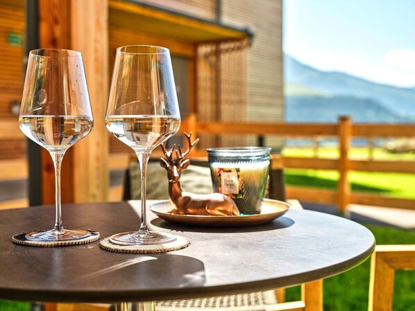 Two wine glasses on a round table with a rustic wooden table and a metal tray with a deer figurine and a candle.