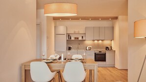 A modern kitchen with a dining area, featuring a wooden table, white chairs, and pendant lighting.