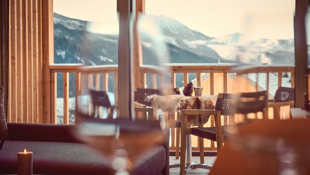 A cozy outdoor seating area with wooden chairs and a table, overlooking a snowy mountain landscape.