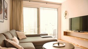 A modern living room with a sectional sofa, a round coffee table, and a flat-screen TV mounted on a wooden shelf.