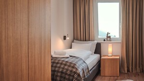 A bedroom with a bed, a nightstand, a window with curtains, and a small decorative item on the windowsill.