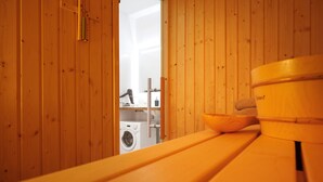 Une salle de sauna en bois avec un banc, un récipient en bois et un sèche-cheveux, que l’on peut apercevoir à l’arrière-plan.