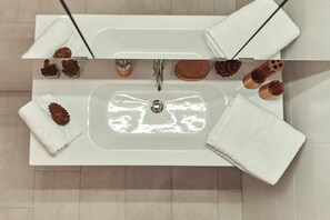 Une salle de bain avec un lavabo blanc, deux serviettes, un miroir et un élément de décoration en forme de pomme de pin.
