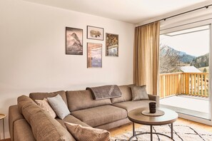 Un salon avec un canapé d’angle marron, une petite table ronde ornée d’une bougie, et une vue sur un balcon doté d’une balustrade en bois.