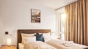 Una habitació d'hotel amb un llit gran, una taula de nit amb una làmpada, un quadre a la paret i una finestra amb cortines.