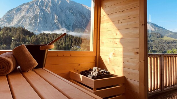 Une cabane en bois dotée d’une terrasse en bois, d’une cheminée et offrant une vue sur une montagne.