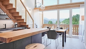Eine moderne Küche mit einer Holztreppe, großen Fenstern und einem Essbereich mit Bergblick.