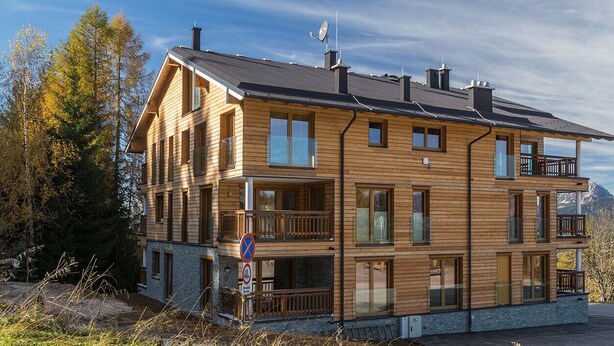 A multi-story wooden chalet with balconies, set against a mountainous backdrop. - Apartment Fastenberg Top 11 (Schladming)