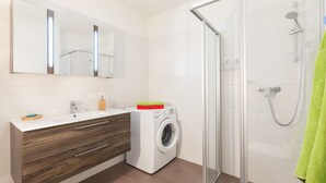 Un baño moderno con lavadora integrada, cabina de ducha de vidrio y un espejo grande sobre el lavamanos.