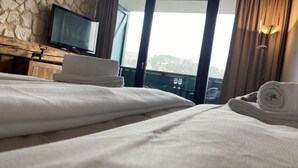 Een hotelkamer met een bed, een televisie op een houten dressoir en uitzicht op het landschap door een glazen deur.