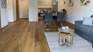 Ett modernt vardagsrum med en grå soffa, ett träbord och en matplats med stolar och ett bord.