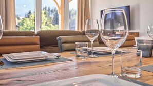 A dining area with a wooden table, clear glassware, and a sofa. - Panorama Lodge Alpine Living 201 (Tauplitz)