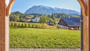 A view through an arched wooden structure with a mountain backdrop, featuring a grassy field and several houses. - Panorama Lodge Alpine Living 201 (Tauplitz)