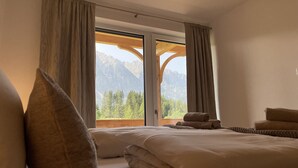 Une chambre avec un grand lit, deux oreillers, une fenêtre avec des rideaux et une vue sur les montagnes.