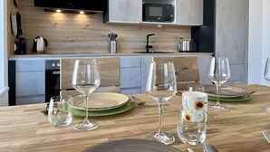 Une cuisine moderne avec des meubles en bois, un four à micro-ondes et un évier. Plusieurs verres à vin et assiettes sont posés sur la table.