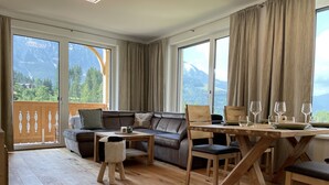 Un salon moderne avec un plancher en bois, un canapé en cuir, une table à manger avec des chaises et de grandes fenêtres avec des rideaux.