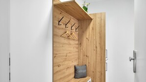 Une pièce moderne et minimaliste, avec un banc en bois, un porte-manteau suspendu et une petite étagère ornée d’une plante.